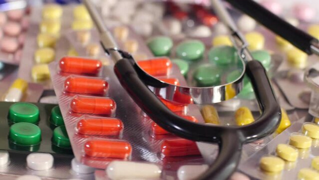 Pharmacy or hospital background with different blister packs of colored capsules, pills, drugs, stethoscope seamlessly spinning close up shot