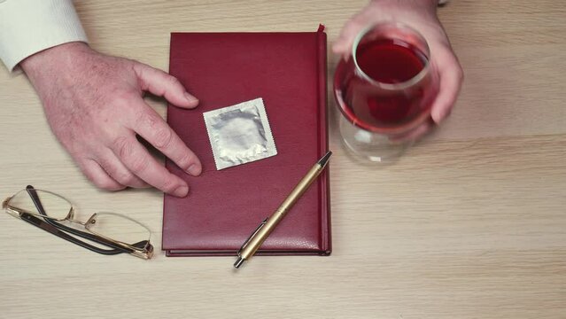 Male hands on the table with a notebook, glasses and a pen take away a condom and a glass of wine