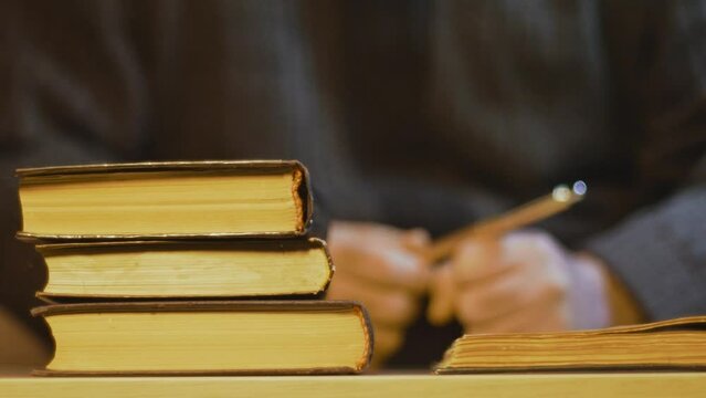 Man puts a pen between the pages of an old book, closes it and puts it on top of a stack of books. Study, education.
