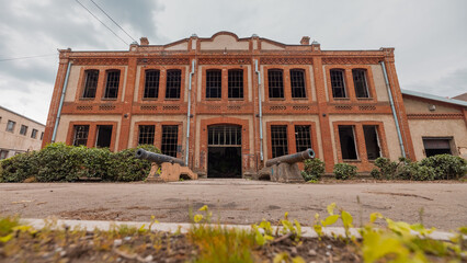 Old industrial warehouse in Kragujevac, Serbia, made of red bricks. Ruined windows and deserted interior on a cloudy day with cannons on the entrance.