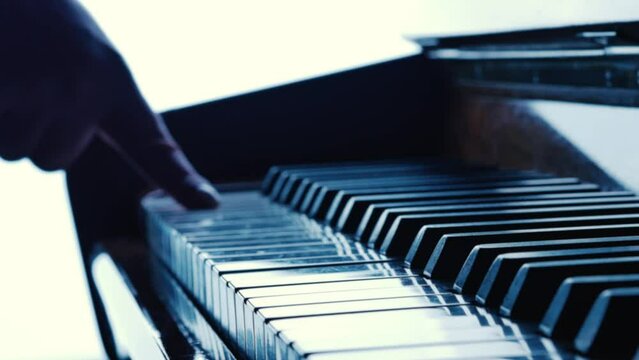 Monochrome shot of the keyboard of a concert grand or upright piano. Female hand runs her finger over white and black keys of a musical instrument. Musician plays chord sounds and scale notes.