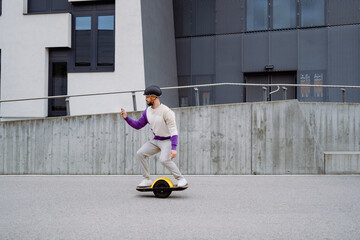 Man rides at electric skateboard and looks at smartphone. Modern building in background