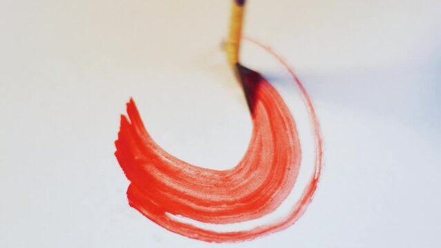 Closeup macro shot of drawing with watercolor paint with a brush red abstract orange swirl on a sheet of white paper