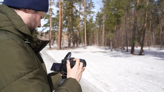 guy photographer takes pictures on camera in the forest. shoot winter forest landscapes. male photographer with beard