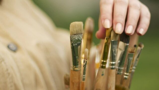 The artist touches the bristles with his fingers and chooses a brush for painting among a bunch of different sizes.