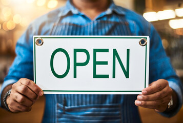 Its official - we just opened. Closeup shot of an unrecognizable man holding up an open sign in his store.