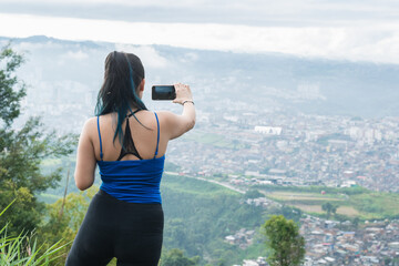 latina woman on the top of a mountain shooting a video of the city of Pereira-Colombia, with her...