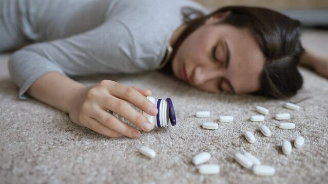 Unconscious woman with pills in her hands lies on the floor