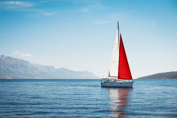 A white yacht with Maltese flag sails at sea against a blue sky and mountains