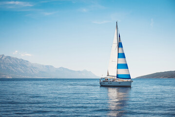 A white yacht with Greek flag sails at sea against the blue sky and mountains - obrazy, fototapety, plakaty