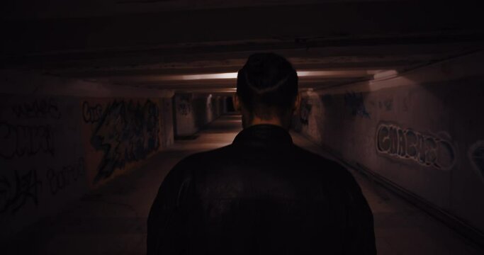 Silhouette of the back of a man walking in a dark underpass. Dark scary movie scene at night city. Handheld camera shot