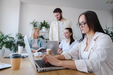 Concentrated female worker is typing on laptop and looking at the screen with serious face