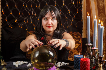 Fortune teller woman brunette in a magic salon reads the future in a crystal ball.