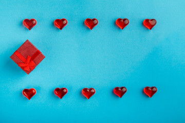 On a blue background, a box with a gift decorated with hearts with red pebbles save a place.