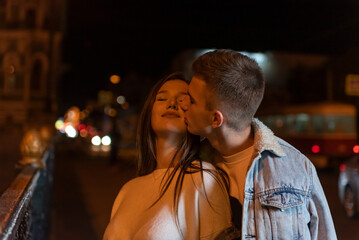 Obraz premium Guy hugs and kisses his girlfriend against evening city backdrop. Date.