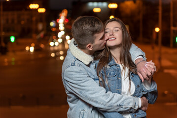 Guy gently hugs and kisses his girlfriend on evening city background. Romantic date.