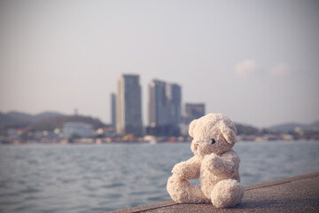 A brown fluffy teddy bear sits on a single bridge looking out to the sea with a copy space background. Lonely, loneliness is pointless.