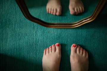two feet with red coral painted toenails looking in mirror