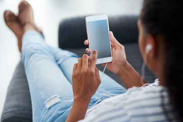 All her free time is spent online. Shot of a young woman wearing earphones while using a cellphone...
