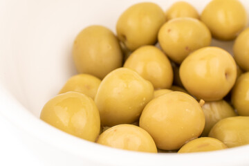 Several green pitted olives in a ceramic white cup, macro, isolated on white.