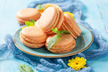 Tasty passion fruits macaroons with flowers on blue table.