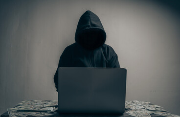 A hacker wears a long-sleeved shirt with a hood covering his head. He was sitting in a dark room...