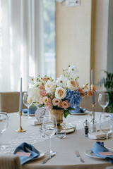 Blue wedding decor. Festive table decorated with flowers on the center, candles, silverware and plates with silk napkins on dusty blue tablecloth