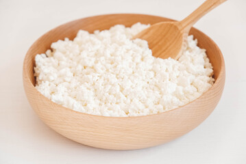 Cottage cheese in a wooden plate with a spoon on a white background