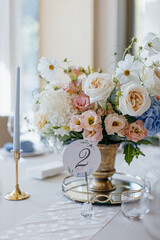 Blue wedding decor. Festive table decorated with flowers on the center, candles, silverware and plates with silk napkins on dusty blue tablecloth