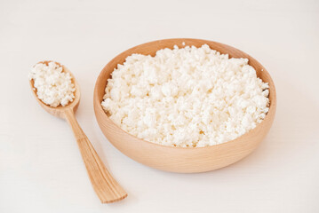 Cottage cheese in a wooden plate with a spoon on a white background