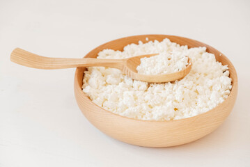 Cottage cheese in a wooden plate with a spoon on a white background