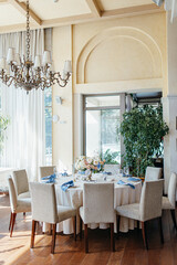 Blue wedding decor. Festive table decorated with flowers on the center, candles, silverware and plates with silk napkins on dusty blue tablecloth