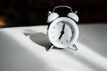 white vintage alarm clock shows 7 am on the dial on a white table close-up