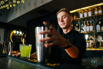 Low-angle view of confident bartender male making colorful alcoholic cocktail standing behind bar...