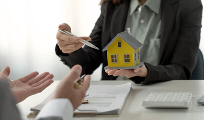 Real estate broker agent presenting and consult to customer to decision making sign insurance form agreement, home model, concerning mortgage loan offer for and house insurance.