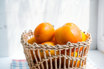 Orange organic tomatoes in wicker basket on a windowsill. Sunlight. Healthy nutrition. Harvest. Minimalistic simple neutral light template. Superfood. Organic eco health care. Vitamin nutrition.