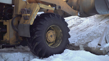 The bulldozer pulls something out with a bucket. CLIP. Close-up on the wheels and bucket of a yellow escalator. In the snow, a bulldozer spins its wheels when it pulls something heavy
