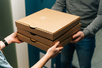 Close-up high-angle view of female customer receiving carton boxes with takeaway at home from delivery man hands. Closeup cropped shot of courier male delivering to woman customer food at home.