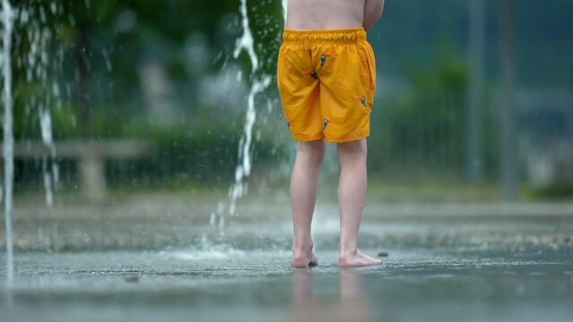 Child running outside on public fountain water kid having fun in summer day