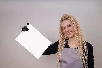 Happy european blonde girl with long hair holding a blank vertical canvas in her hands, poster mockup with empty frame. A specialist in the field of manicure, hairstyles, tattoo holds a certificate.