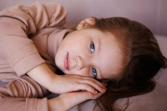 Portrait of 6-year-old little girl laying on her back in casual outfit, on sofa at home. Female child pretty face with beautiful deep eyes. Cute baby girl smiling. Relax and peace. Turtleneck clothes