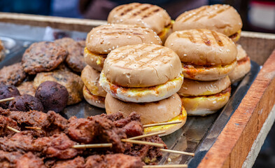 Delicious burgers and grilled chicken sticks on a street food market close up