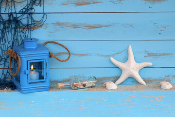 Laterne, Seestern und Flaschenpost vor einer blauen Holzwand.