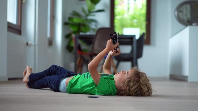 Small boy lying on floor at home playing with toys child plays by himself