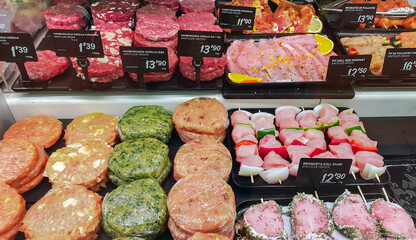Meat section with fresh beef and chicken chops, skewers with vegetables on the counter in a food...