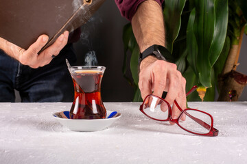 Man reading a book and a cup of hot turkish tea on the table