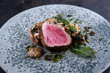 Modernes Style traditionell gebratenes dry aged Angus Filet Medaillon vom Rind mit gefüllten Champignon Köpfen und Trüffel Creme serviert als close-up auf einem Nordic Design Teller 