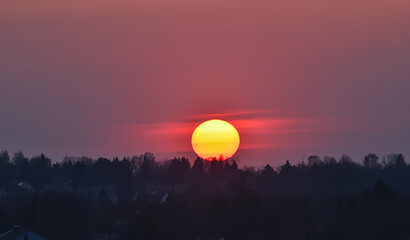 Big sun sinks below the horizon. Colorful sunset in the mist.
