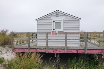 Fototapeta na wymiar Small lifeguard shack with a large porch on a beach withe a beach closed sign