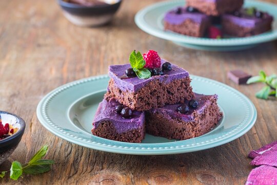 Dessert, sliced chocolate brownies with a layer of ricotta or cream cheese and blueberry puree on a green plate on a brown wooden background. American cuisine.